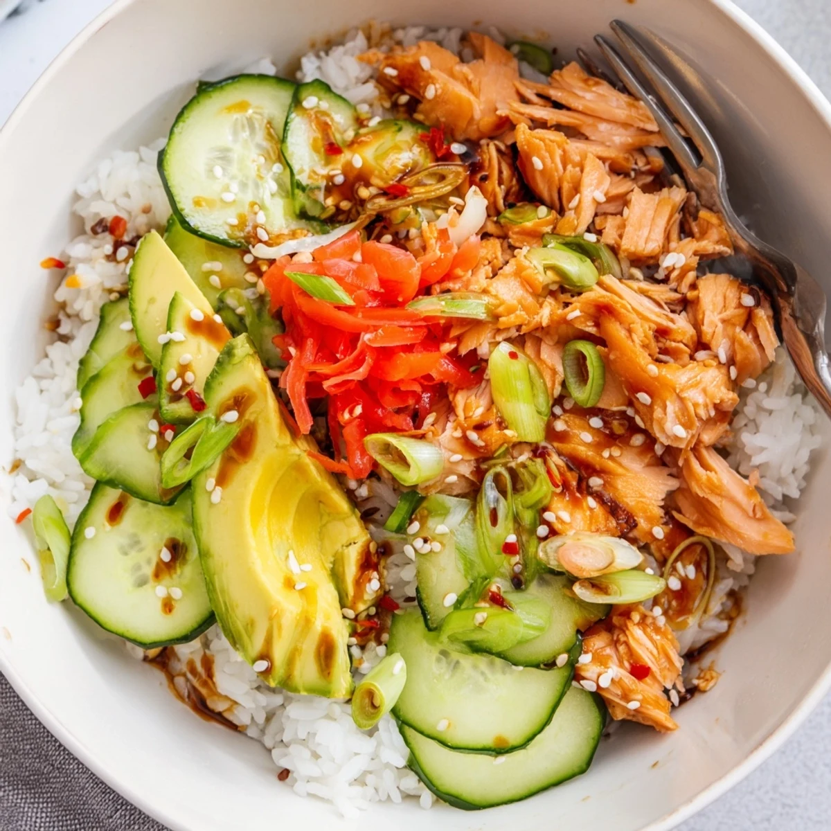 Bowl of vibrant leftover salmon and rice, topped with fresh avocado and cucumber.  