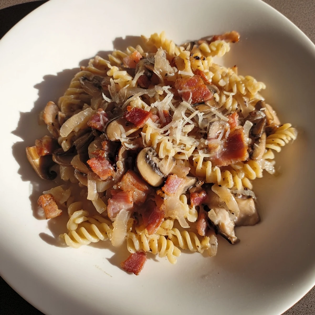 Golden-brown crispy bacon coats the fusilli with onions and mushrooms, perfect for dinner.