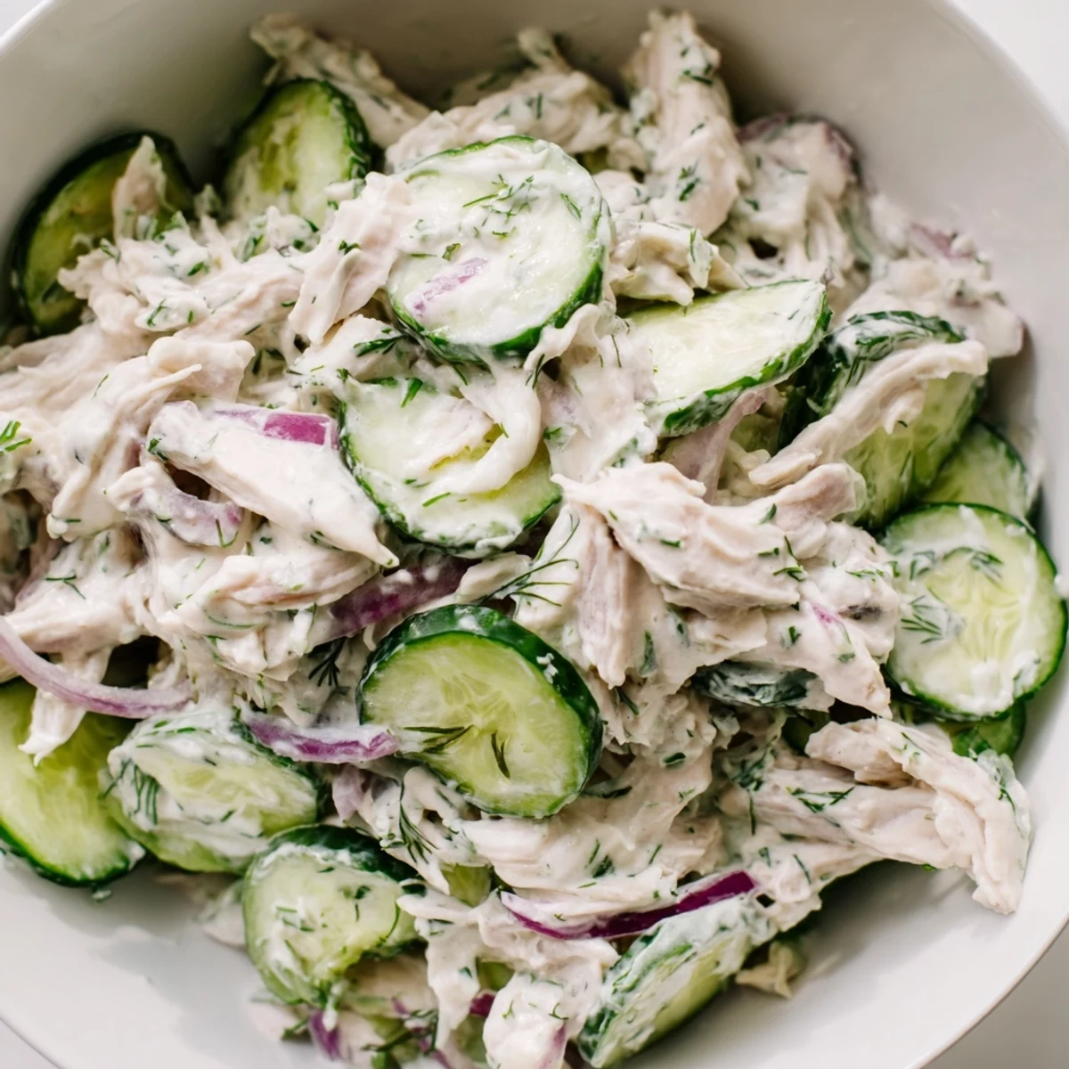 Close-up of Creamy Cucumber Chicken Salad showing creamy yogurt dressing coating chunks of chicken and vegetables in a rustic setting.