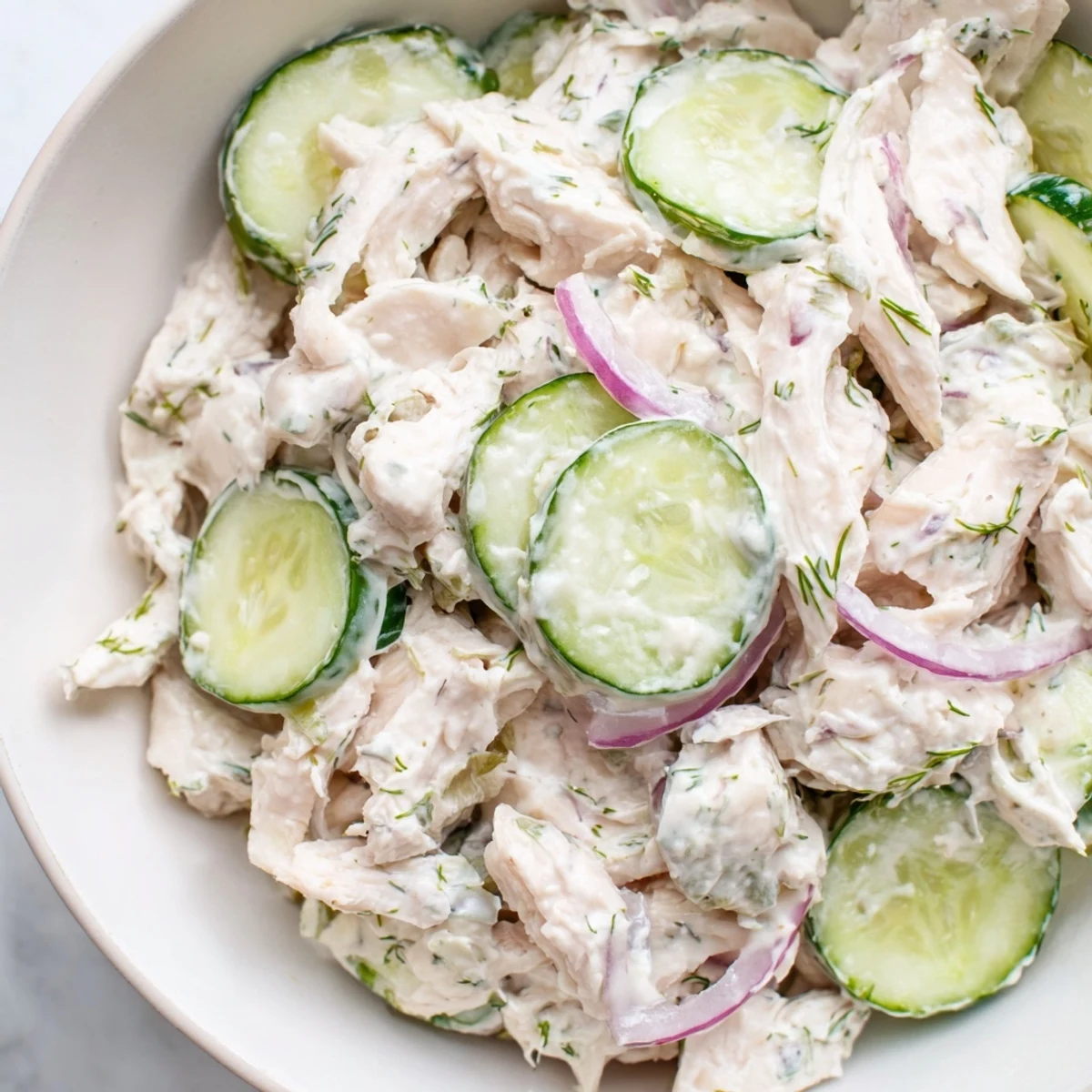 Creamy Cucumber Chicken Salad served in a chilled bowl, topped with green onions and lemon wedges for a refreshing meal.