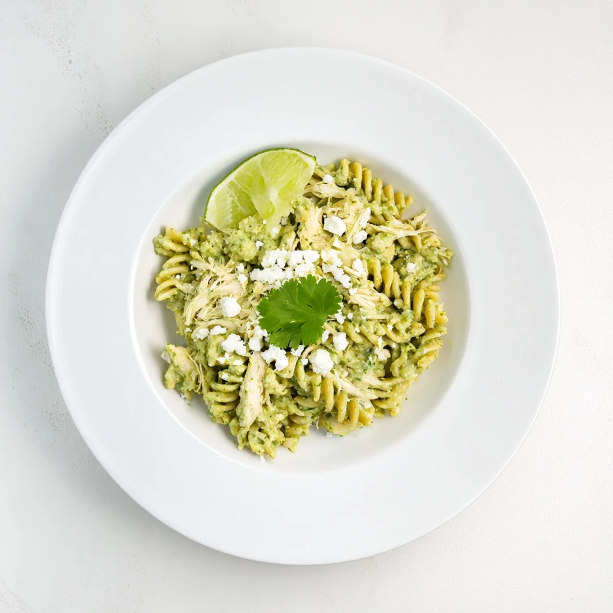 A vibrant bowl of Cilantro Lime Chicken Pasta, featuring rotini and shredded chicken coated in a bright green yogurt sauce.