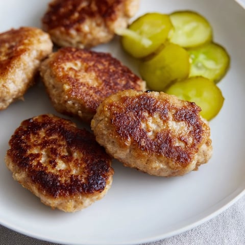 Golden-brown Danish Frikadeller meatballs, pan-fried to perfection, are ready for serving with pickles.