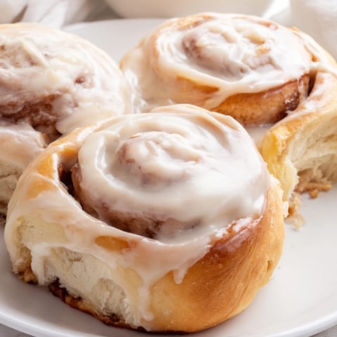 Warm, golden Pillow Soft Cinnamon Rolls fresh from the oven, drizzled generously with creamy glaze.