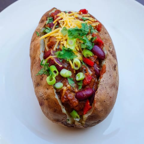 A close-up of Chili-Style Baked Potatoes overflowing with chili, cheese, and fresh green onions.