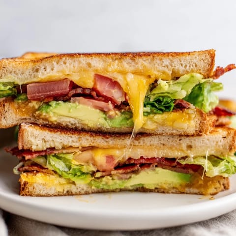Avocado BLT Grilled Cheese sandwich cut diagonally, revealing layers of gooey melted cheese, avocado, lettuce, tomato, and crunchy bacon between golden toast.