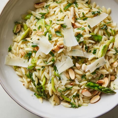 A vibrant spring Asparagus Lemon Orzo Salad served in a white bowl, garnished with fresh parsley and pine nuts.