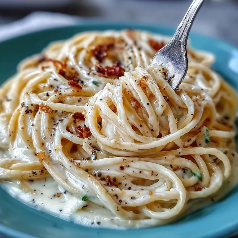 Close-up view of Cacio e Pepe on a fork, revealing the rich, savory cheese sauce clinging to the pasta with aromatic black pepper specks.