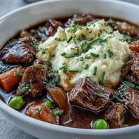A steaming bowl of lightened Irish beef stew with tender lean beef and hearty vegetables, served over creamy cauliflower mash for a healthy twist.  