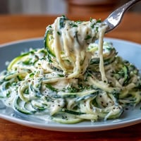Creamy cottage cheese Alfredo sauce drizzled over fresh zucchini noodles, garnished with parsley and Parmesan.  
